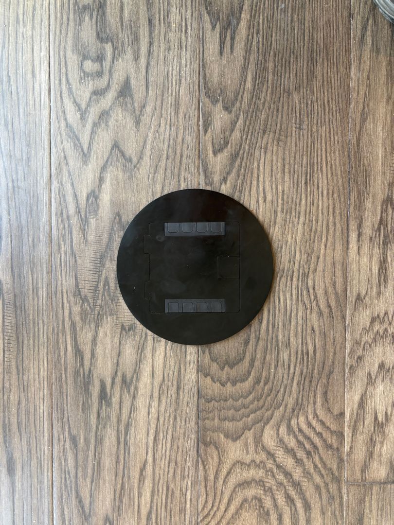 Black circular object mounted on a light wood-grain wall.
