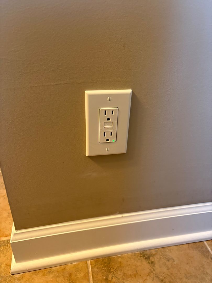Wall outlet with a white electrical faceplate on a tan wall above white baseboard trim.