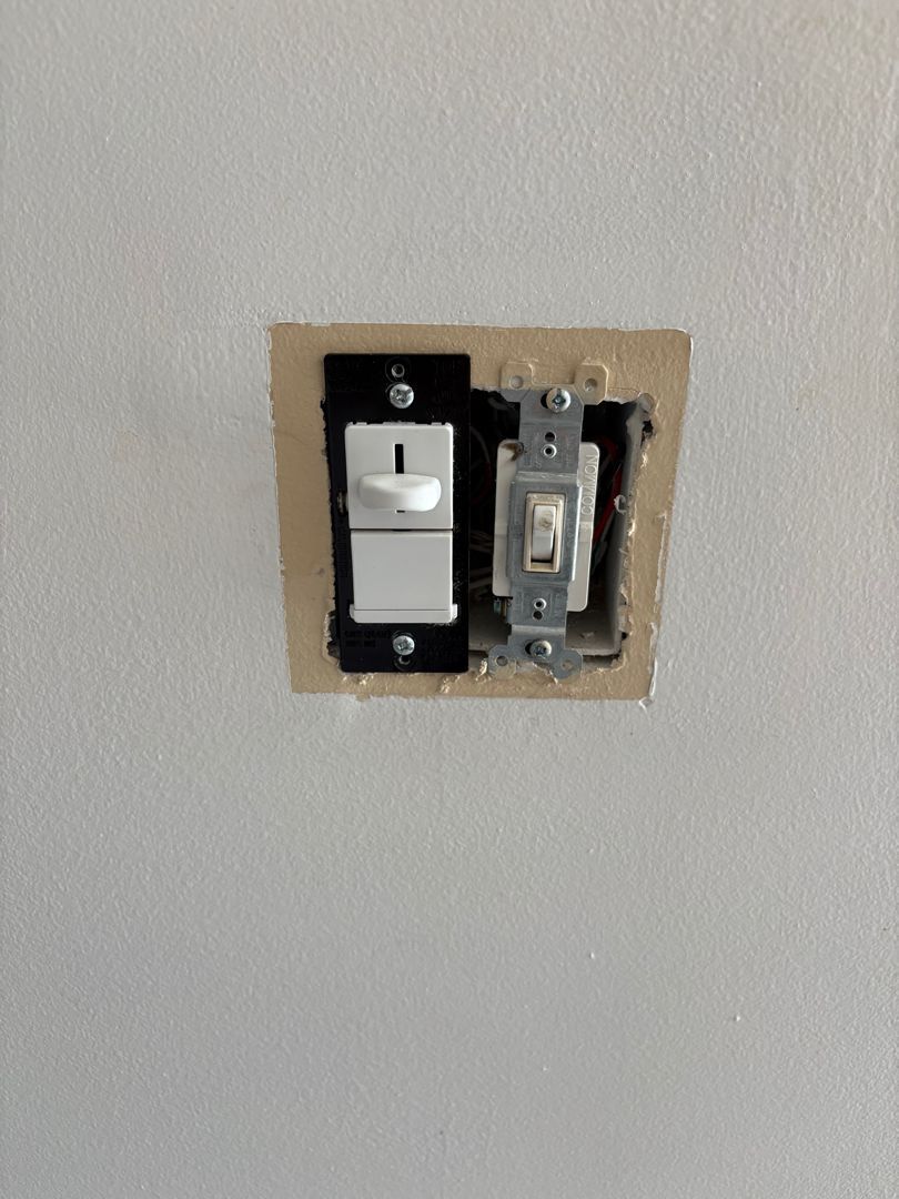 Wall with a two-gang light switch opening, one white switch installed and one exposed switch on the right