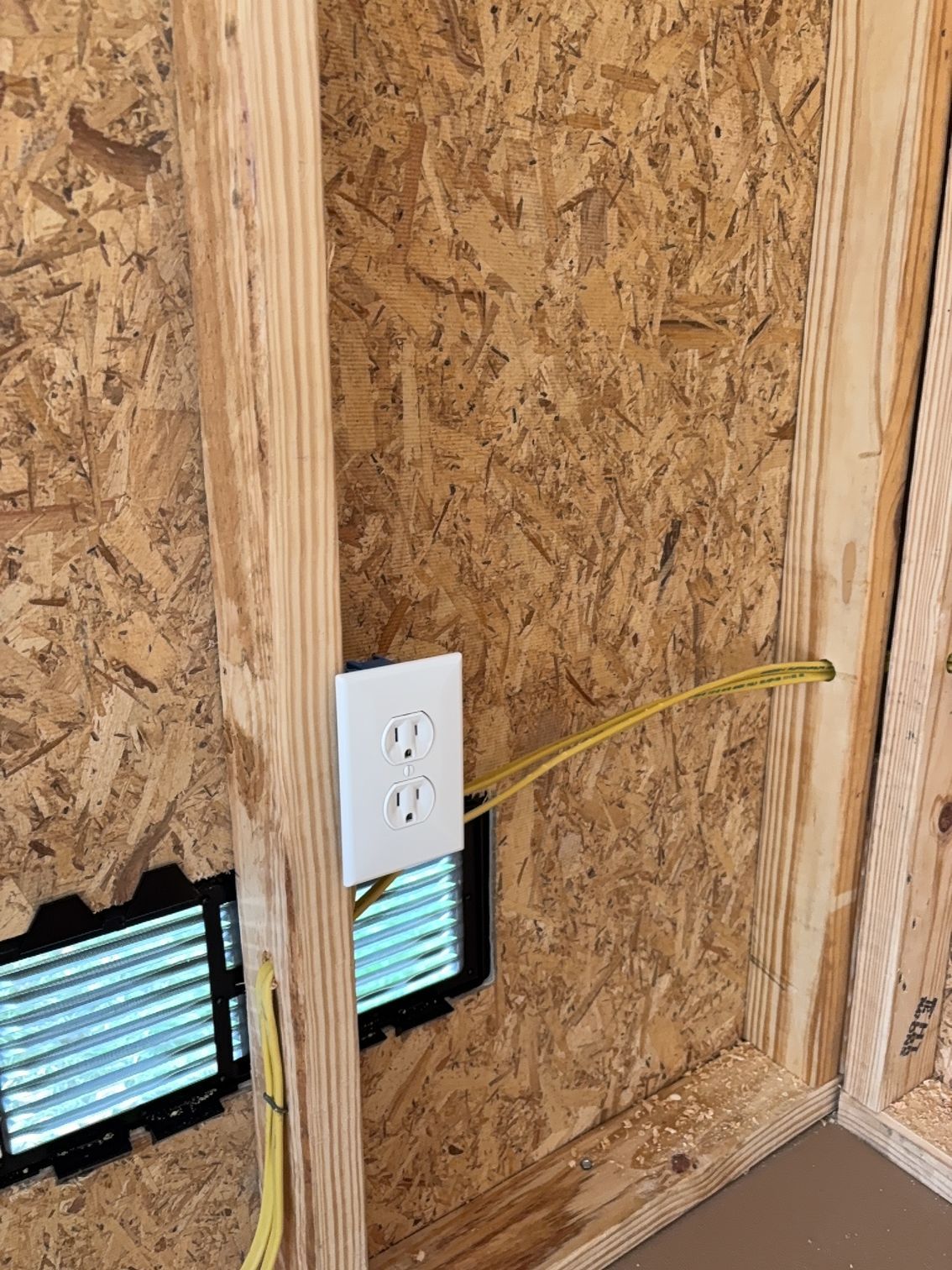 Electrical outlet on plywood wall near small windows, with yellow cable running across the frame.