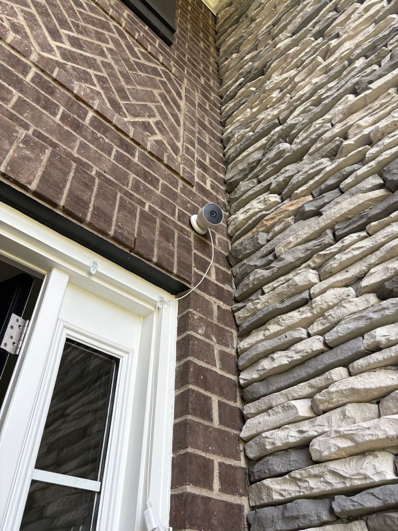 Brick building corner with white-framed window and a small security camera mounted near the top.
