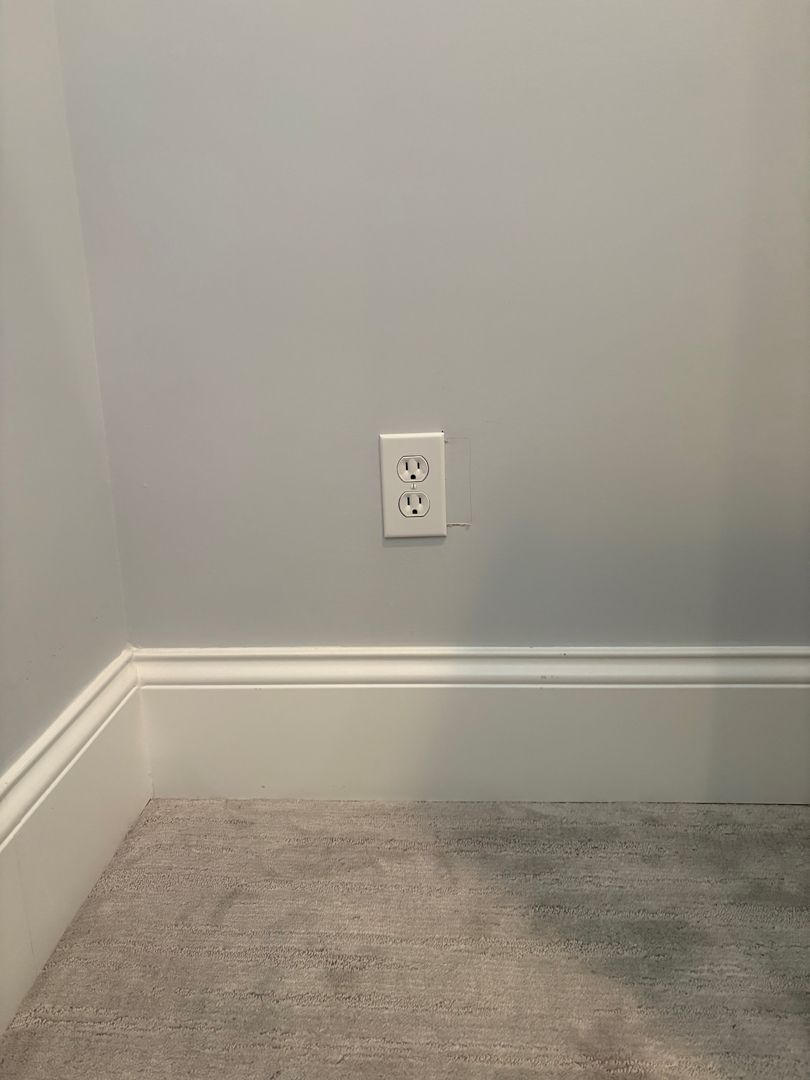 Empty gray room corner with white electrical outlet and carpeted floor