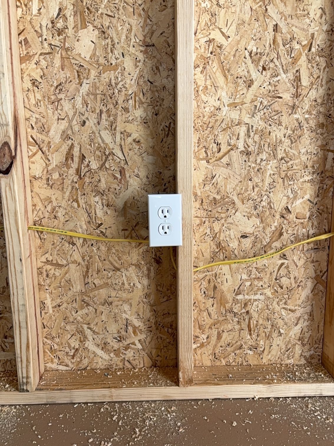 OSB wall with centered electrical outlet and yellow measuring tape across studs