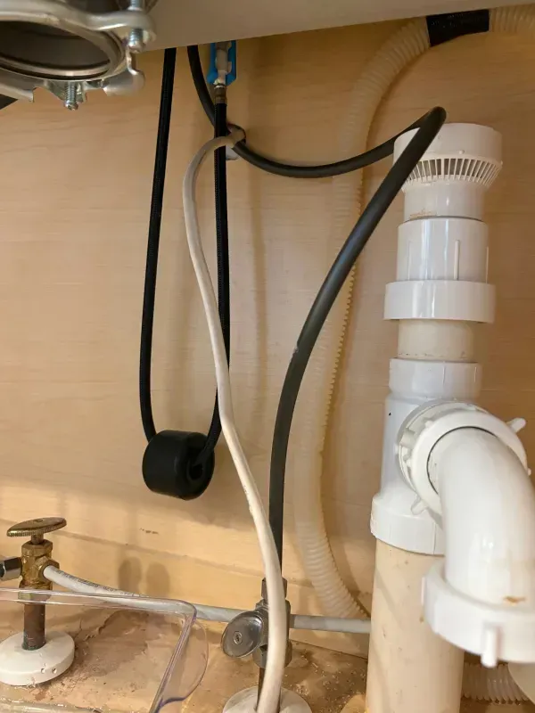 Under-sink plumbing with white drain pipe, black hose, and water shutoff valve in a cabinet