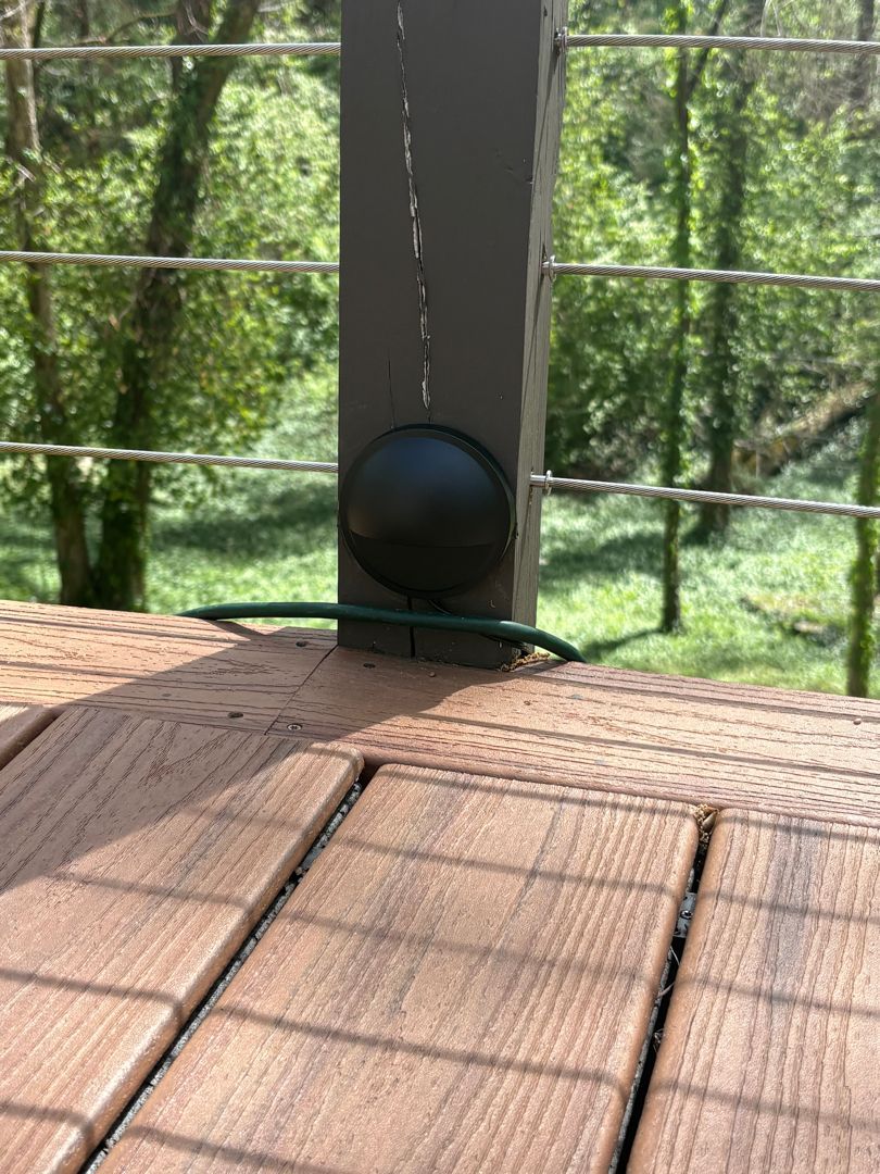 Black spherical object on a wooden deck beside a post, with a green railing and trees in the background
