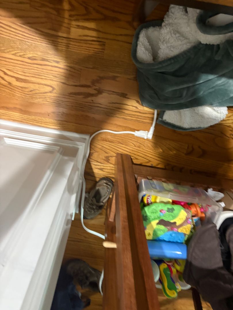 Wooden floor beside a white fridge and open drawer, with a green bag and scattered household items.