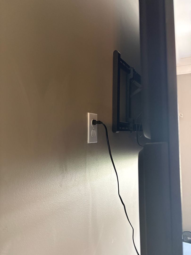 Wall-mounted TV with a dangling black cable beside a power outlet in a hallway.