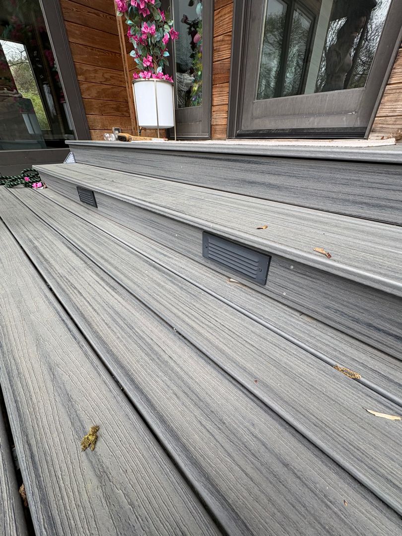 Gray outdoor deck stairs with a potted pink flower near the top step