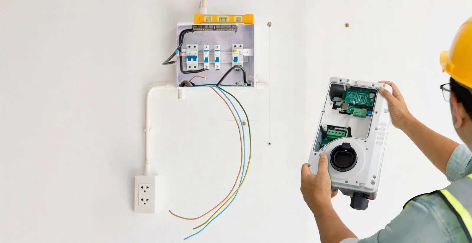 Electrician installing wiring in a wall-mounted electrical box beside exposed cables and outlet.