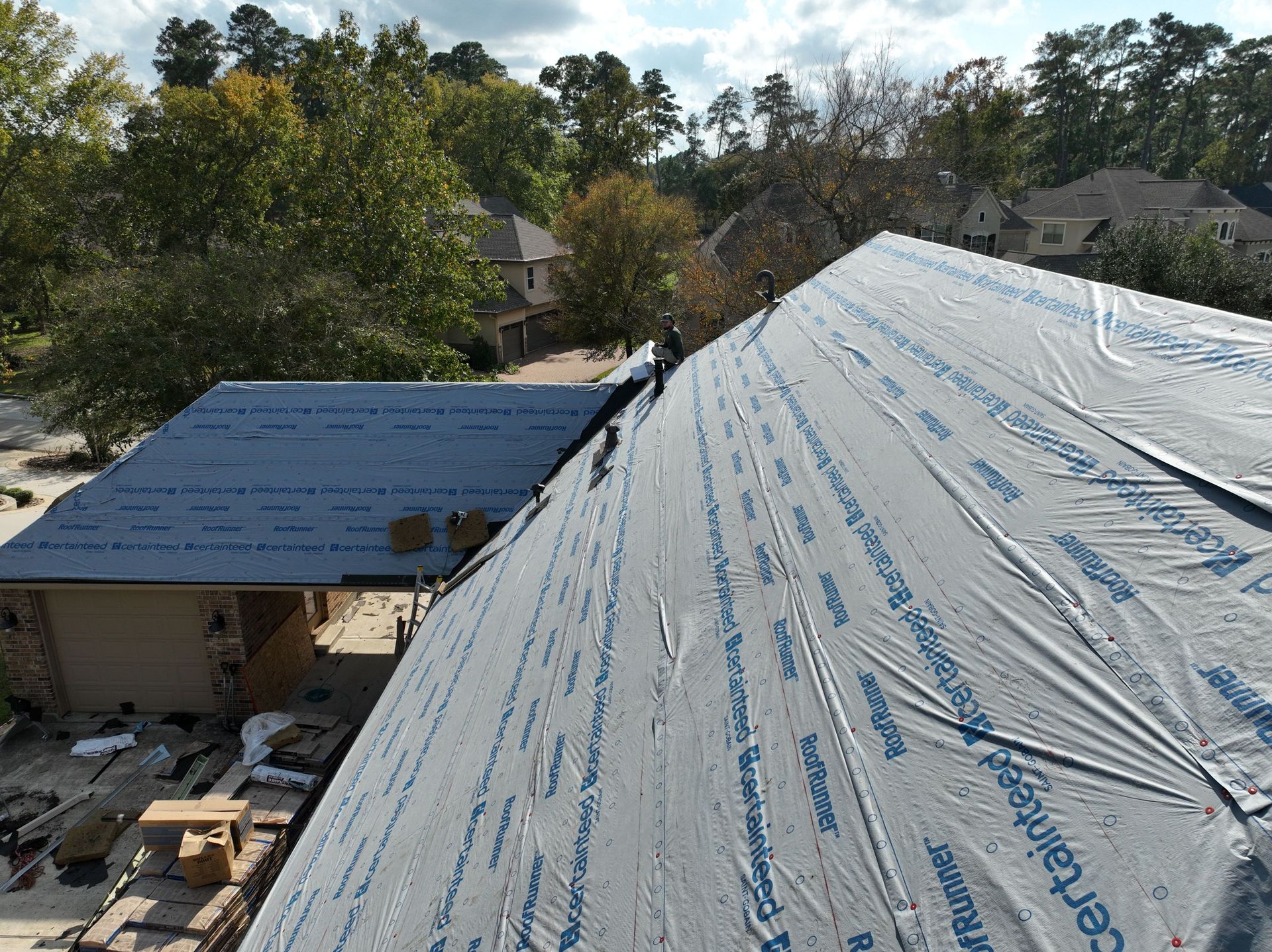 Overhead view of several dark gray shingled roofs of houses in a neighborhood.