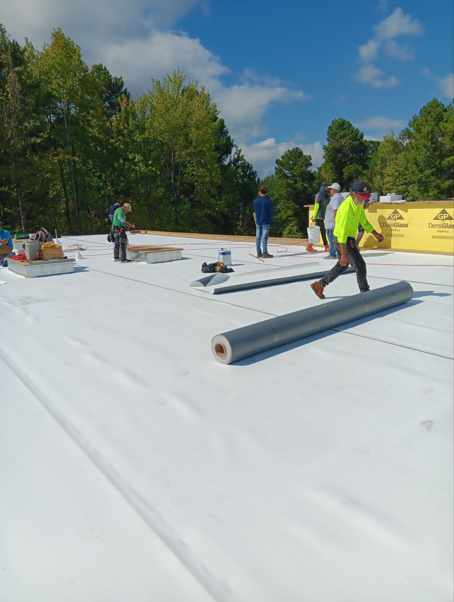 Construction workers installing a white roofing membrane on a sunny day.