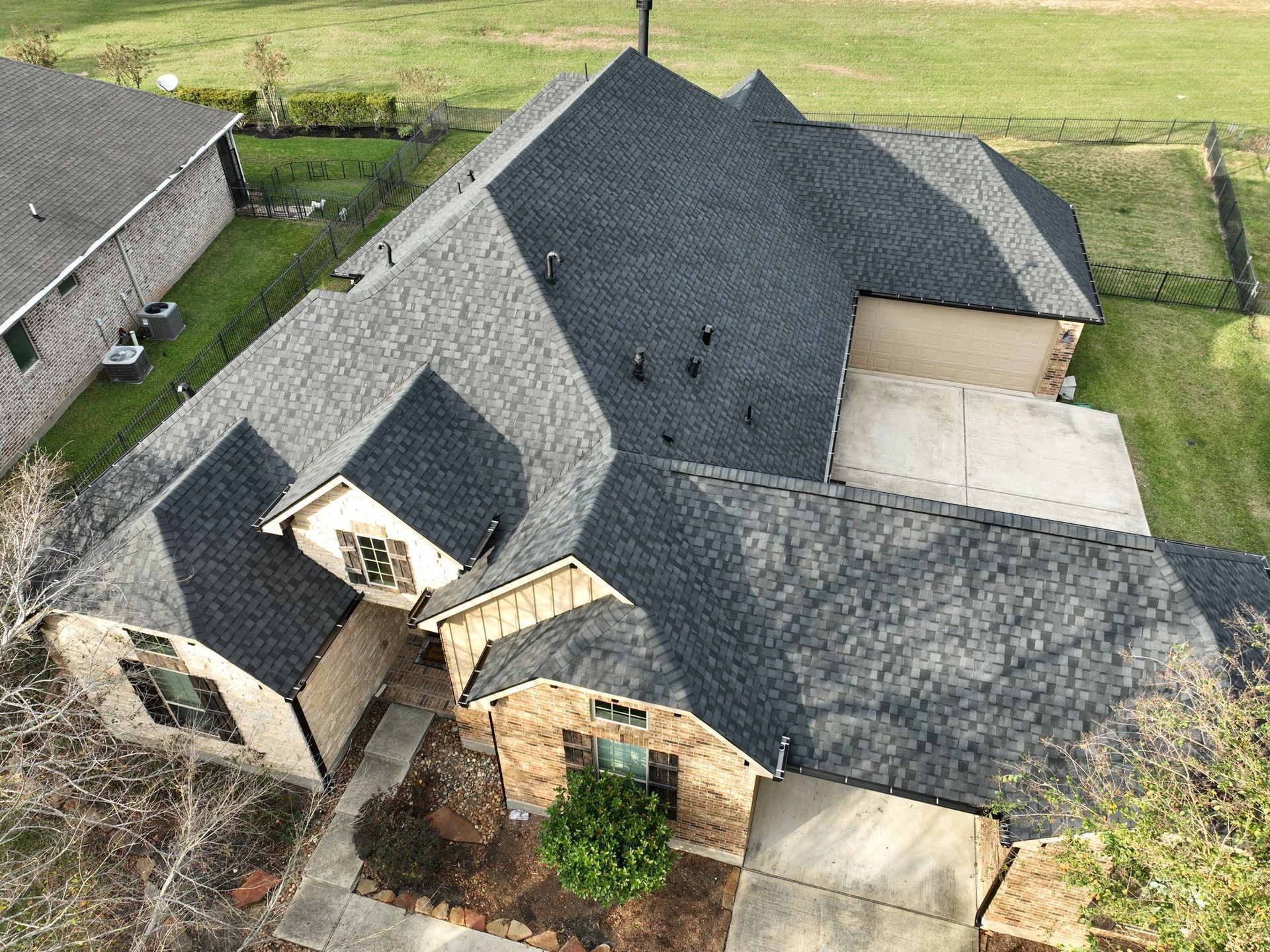 Overhead view of several dark gray shingled roofs of houses in a neighborhood.