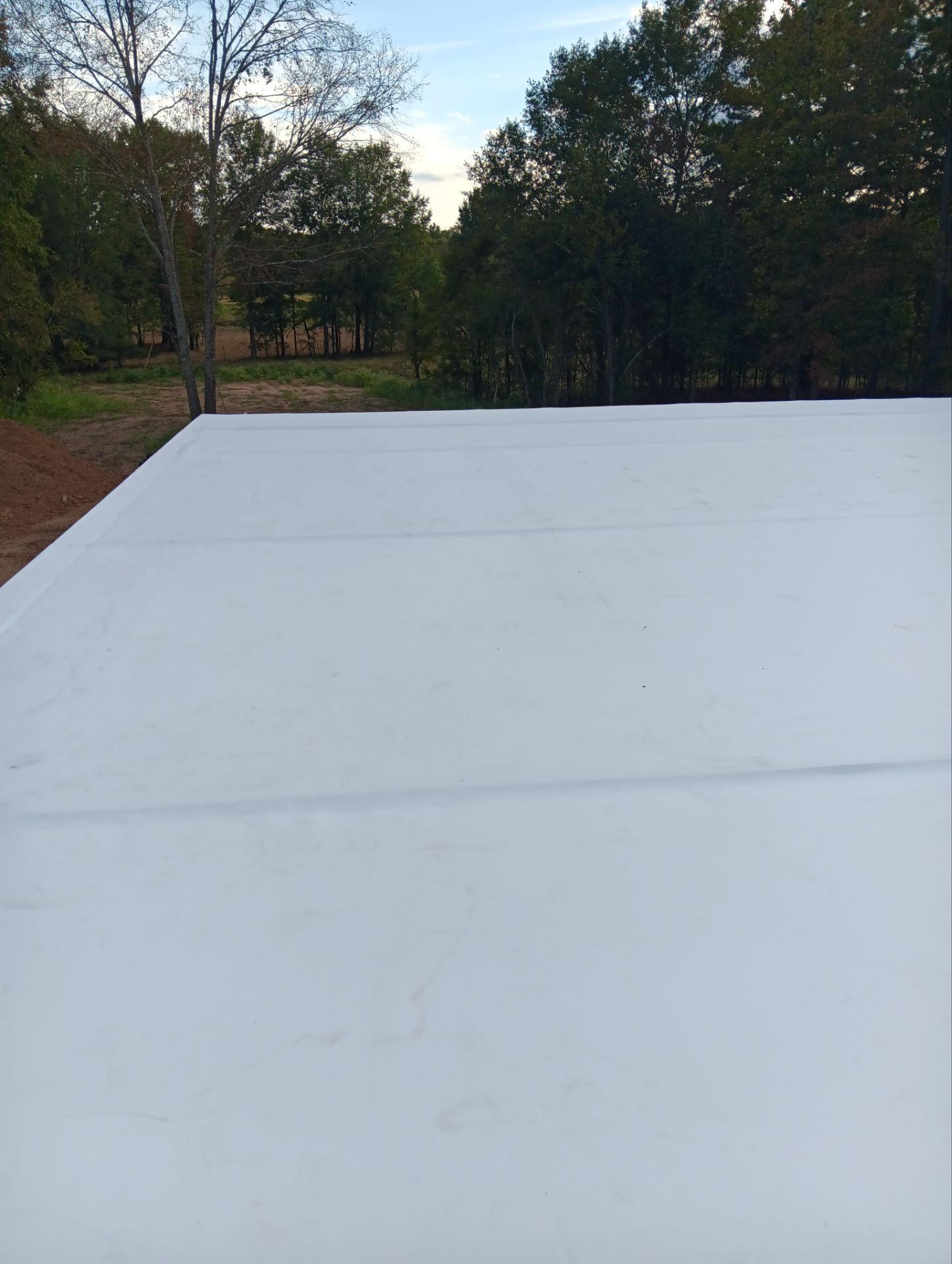 White, flat surface with visible seams, overlooking a wooded area under a blue sky.