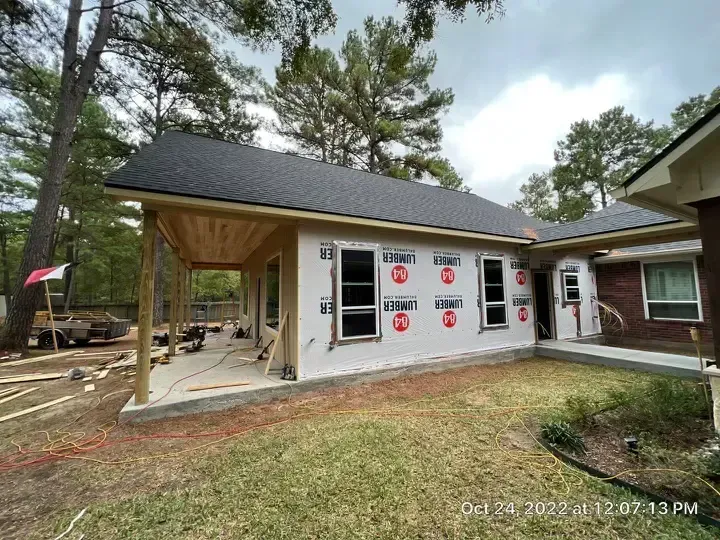 Exterior construction: New room addition with windows under a dark roof, adjacent to existing brick house.