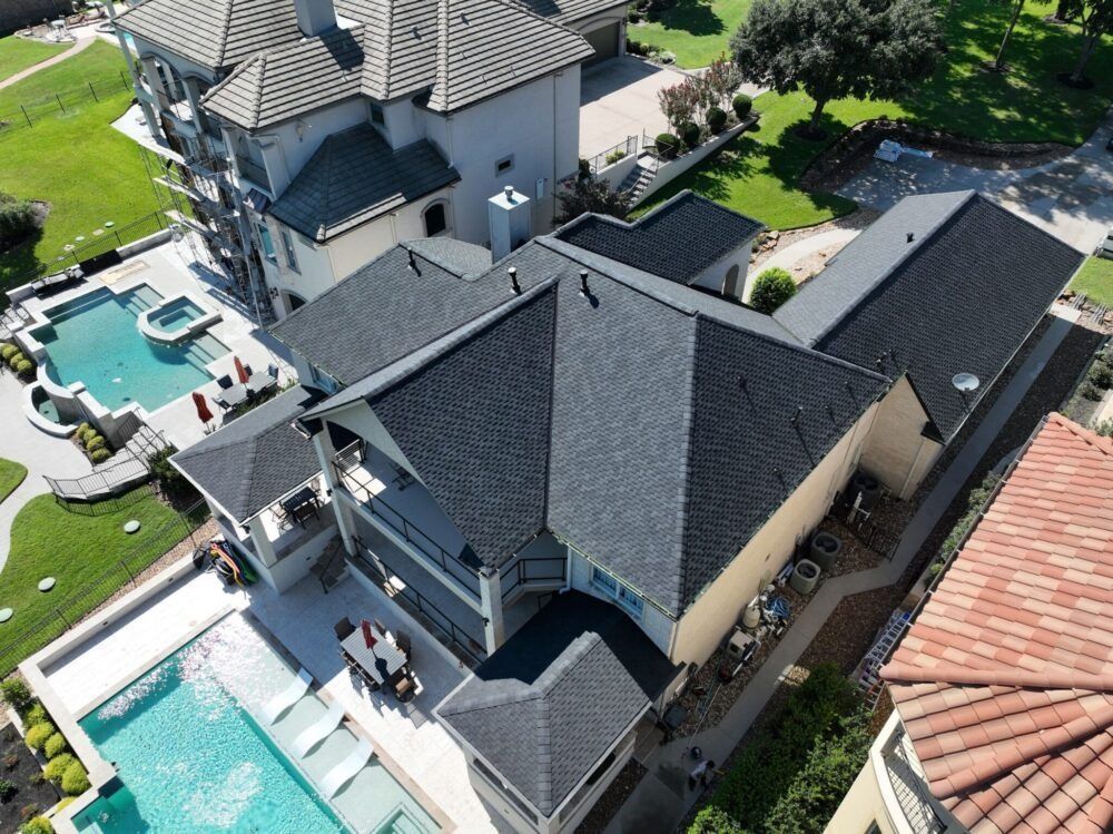 Overhead view of a large house with a black roof, swimming pool, and manicured lawn.