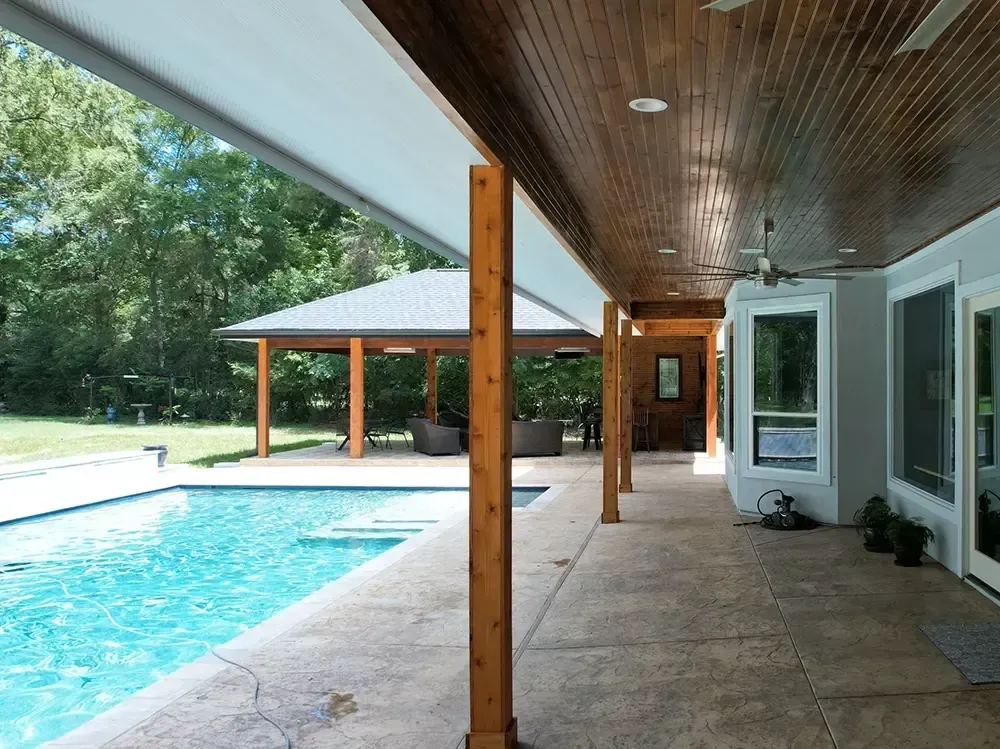 Poolside patio with wooden beams and ceiling, looking out to pool and gazebo.