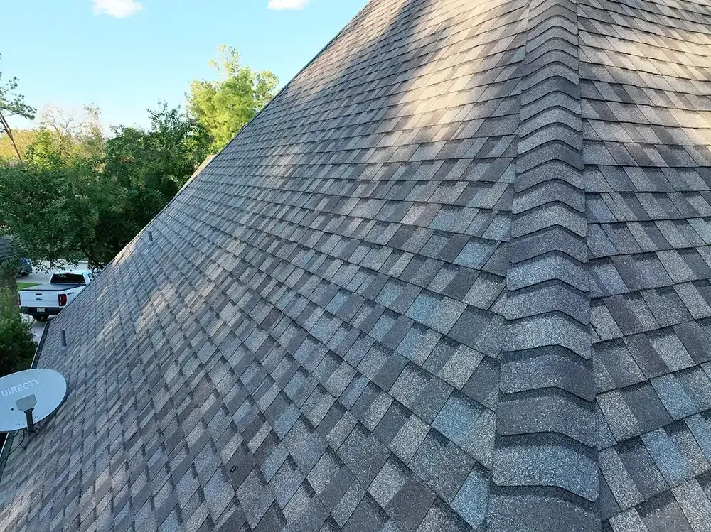 Gray asphalt shingle roof on a house, angled view. A white truck and trees are in the background.