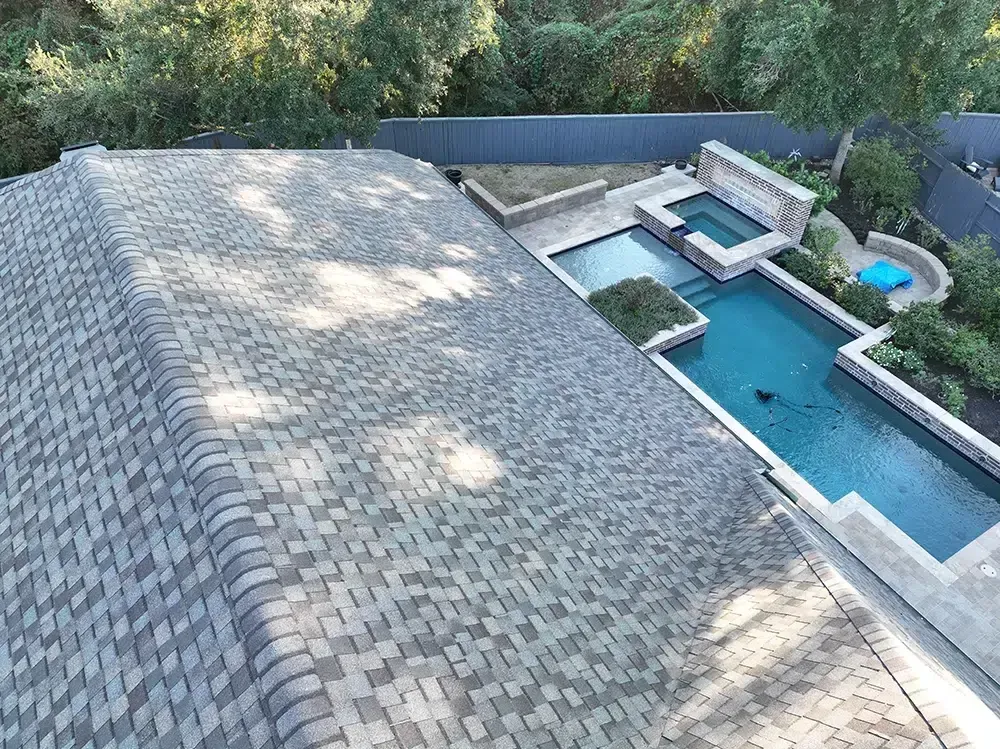 Overhead view of house roof with gray shingles, next to a backyard with pool.