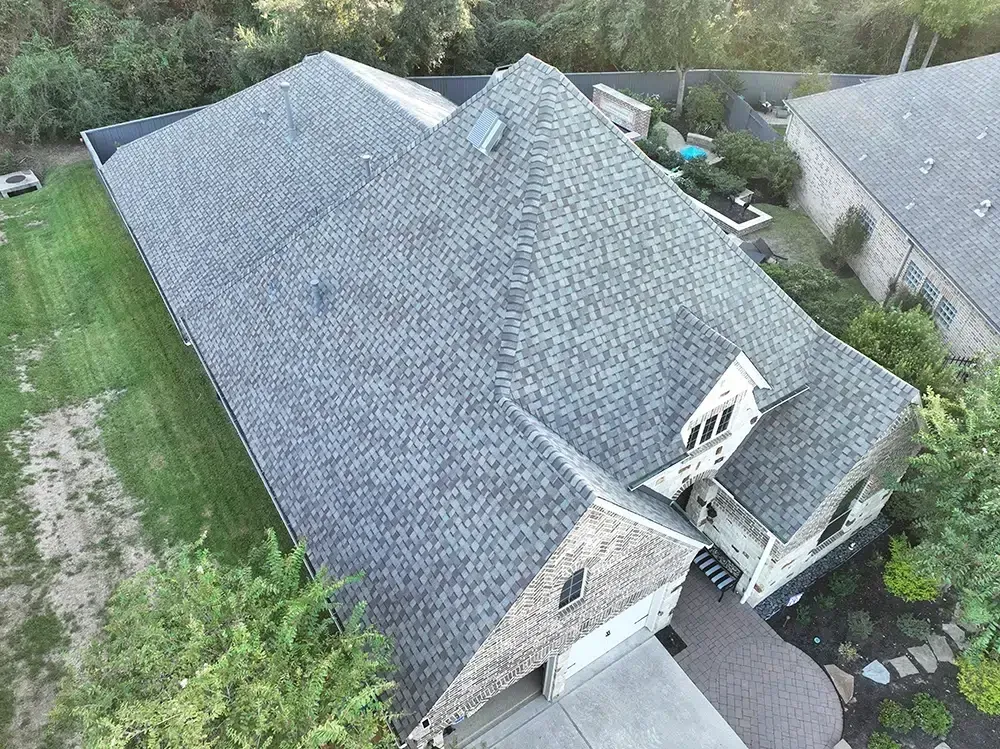 Aerial view of a gray asphalt shingle roof on a house with a surrounding green yard.