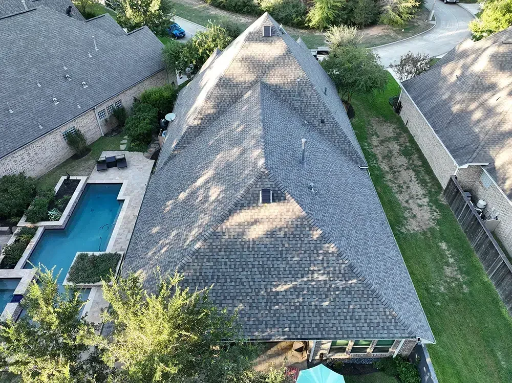 Aerial view of a house with a large, angled roof, swimming pool, and trees.