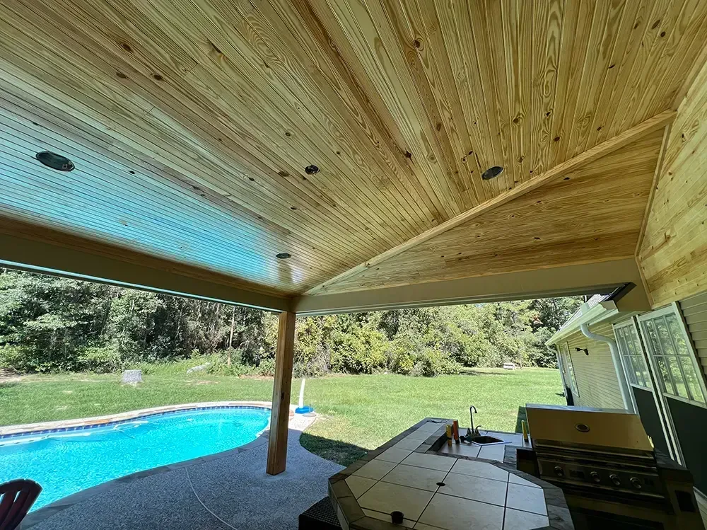 Poolside covered patio with wood ceiling, recessed lights, and view of yard and pool.