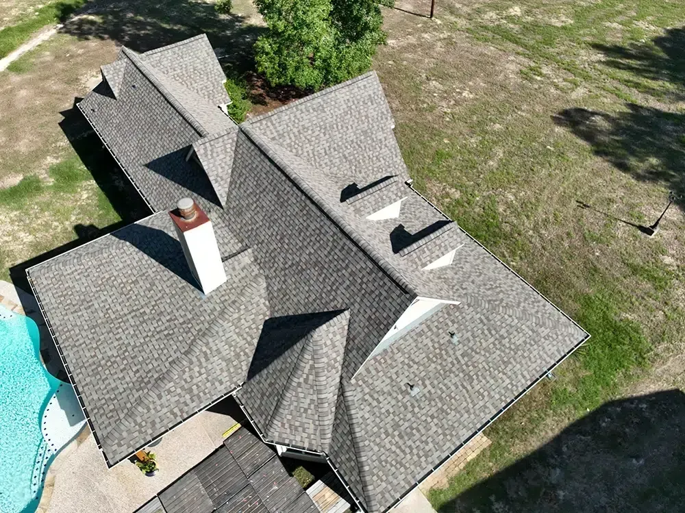 Overhead view of a house with a gray shingled roof, chimney, and a pool.