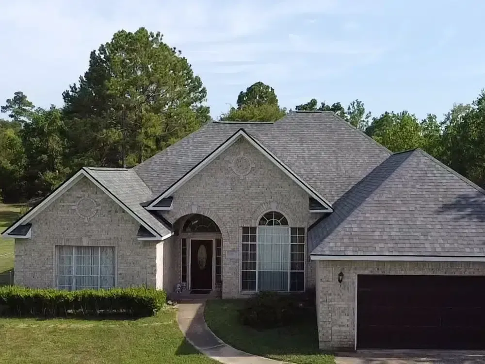 A brick house with a gray roof, arched front door, and attached garage sits on a green lawn.
