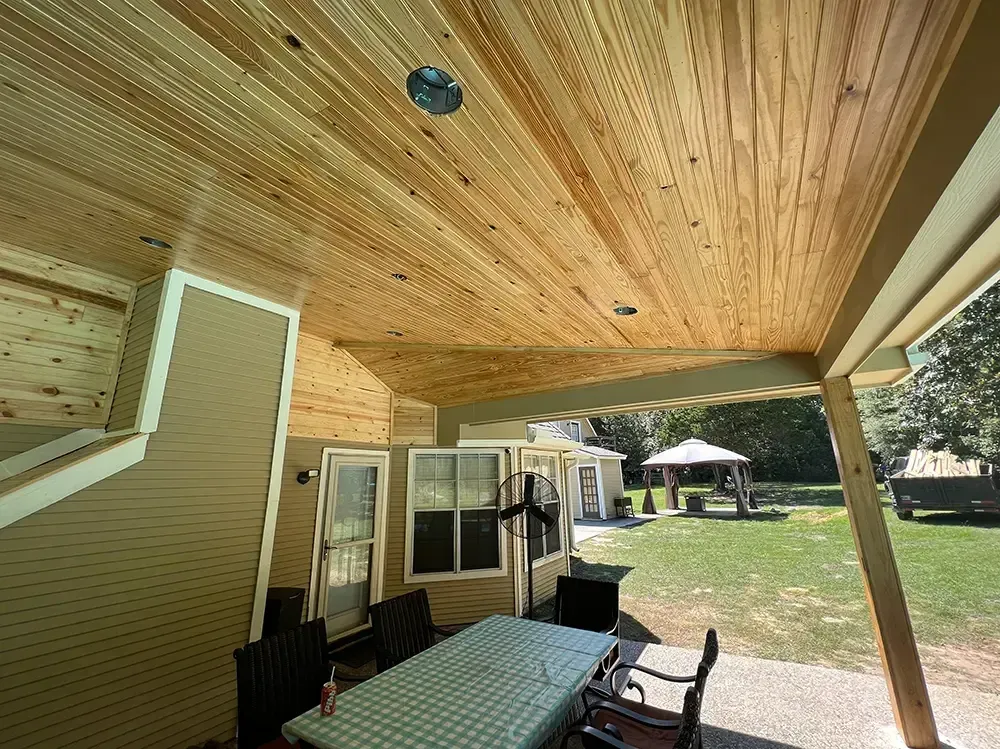 Patio with wooden ceiling, table with green tablecloth, chairs, and view of backyard with gazebo.