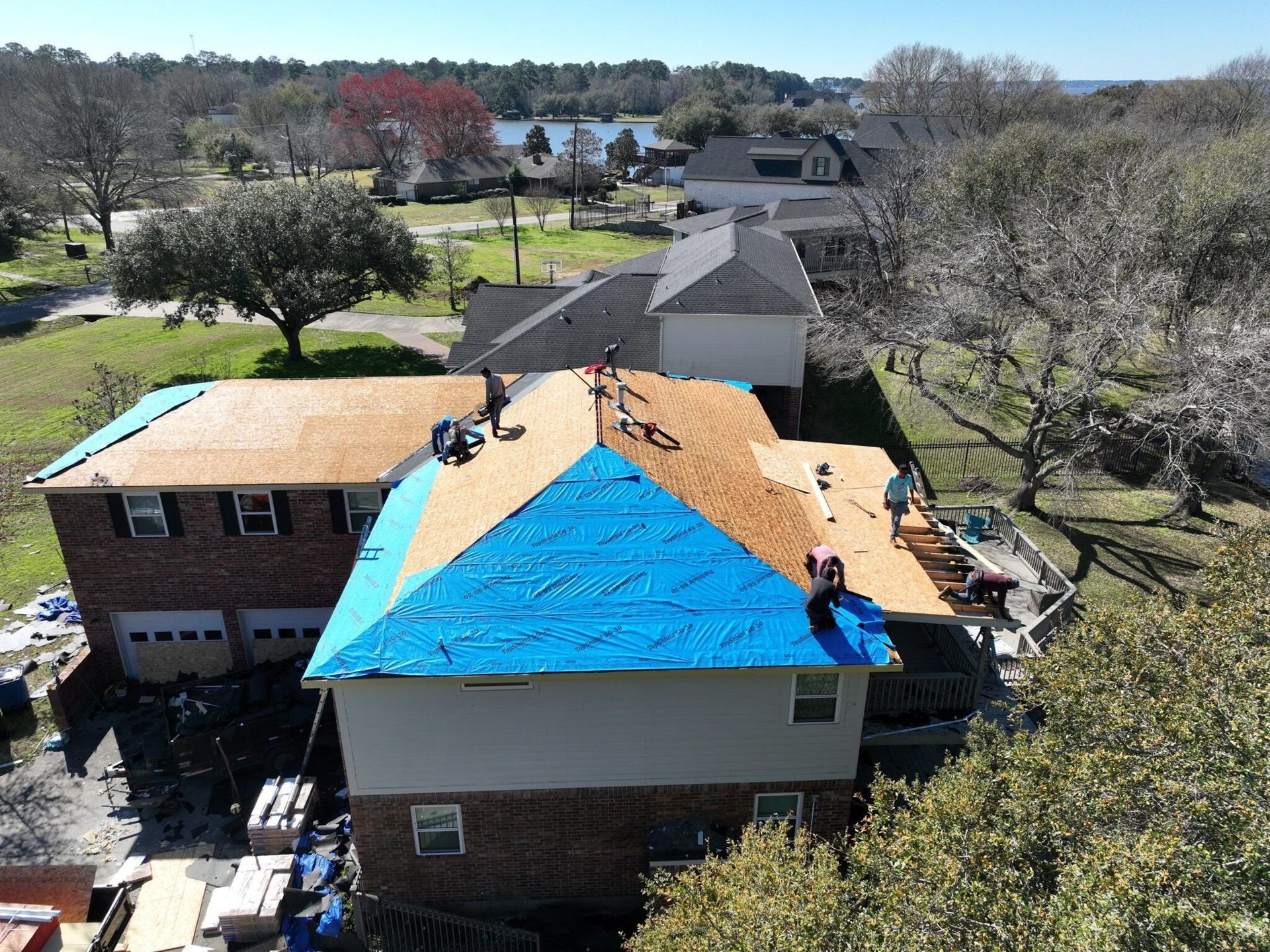 Roofers installing new shingles on a house roof partially covered with blue tarp. Sunny day, residential setting.