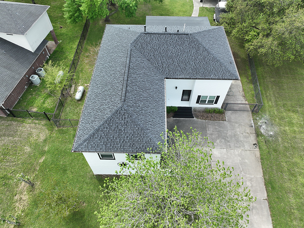 An aerial view of a white house with a dark gray roof surrounded by green grass and a concrete driveway.