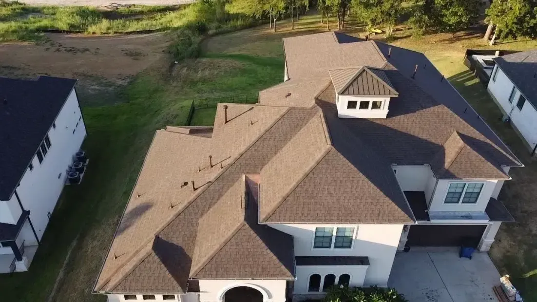 Aerial view of a brown-roofed house with multiple rooflines, a garage, and light-colored siding.