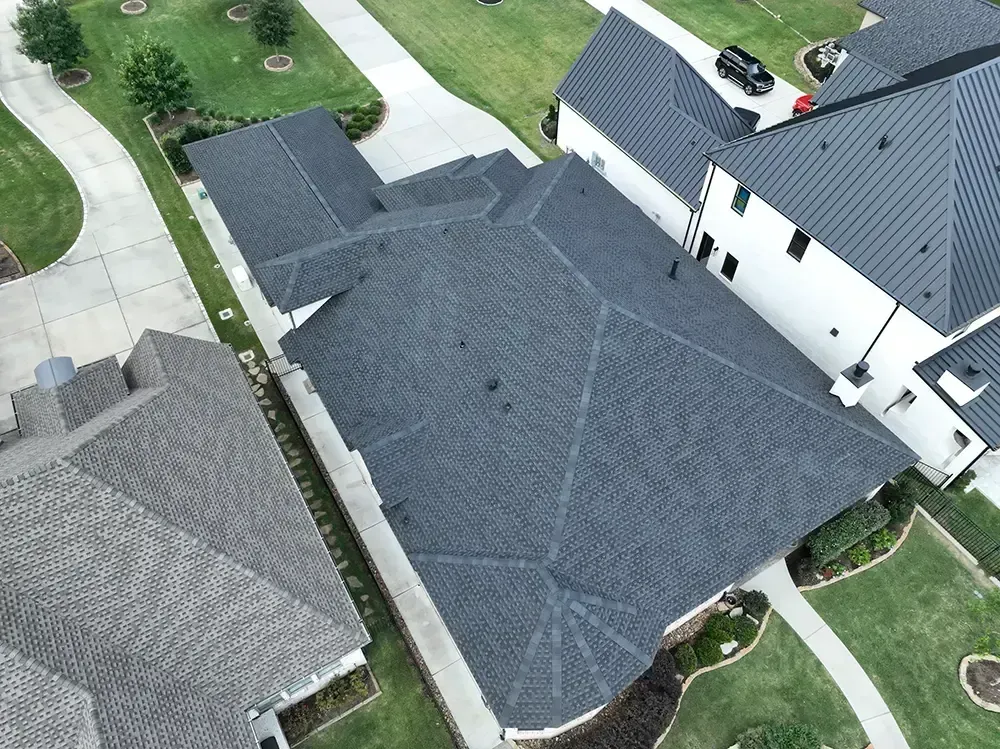 Overhead view of several dark gray shingled roofs of houses in a neighborhood.