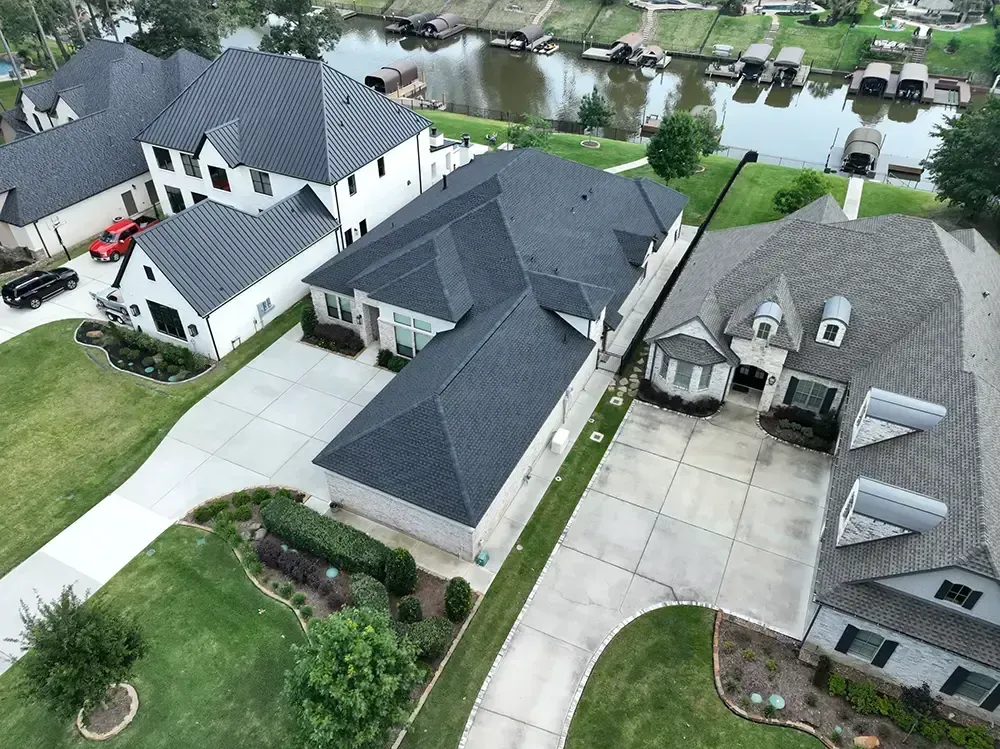 Aerial view of upscale homes with dark roofs near a lake and boat docks.