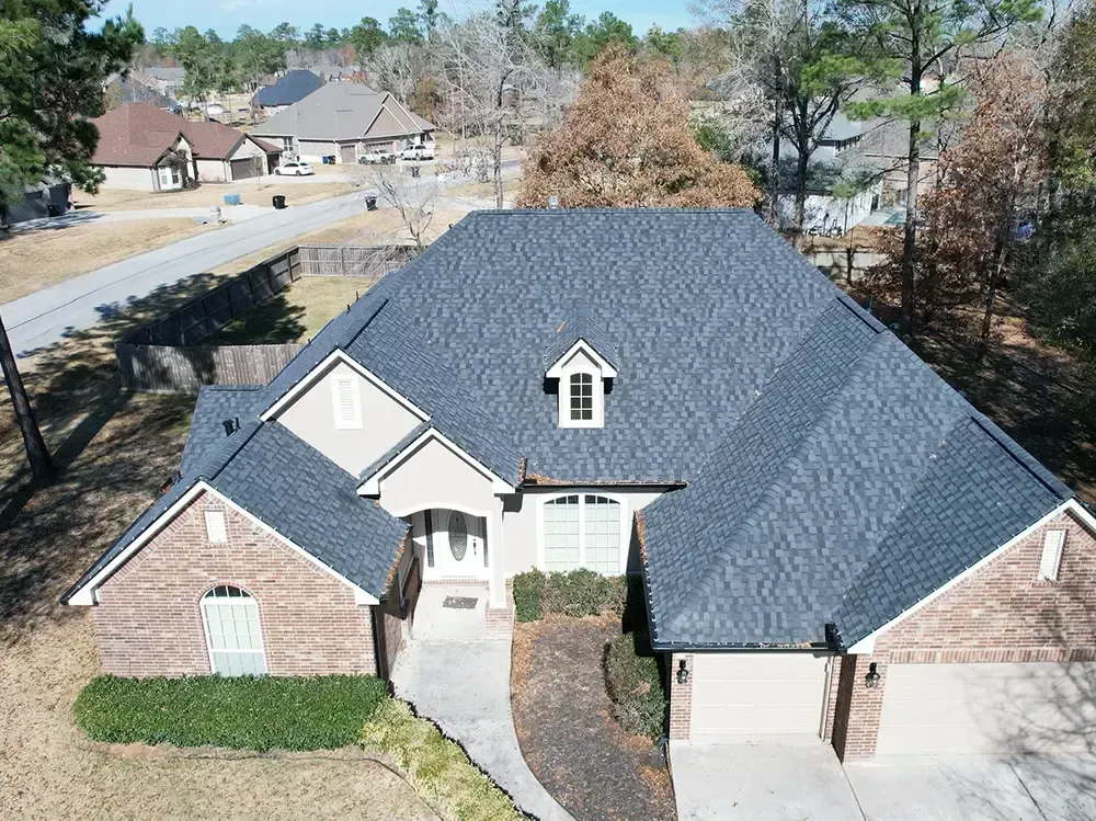 A house with a dark gray roof and brick facade; driveway leads to the front door.