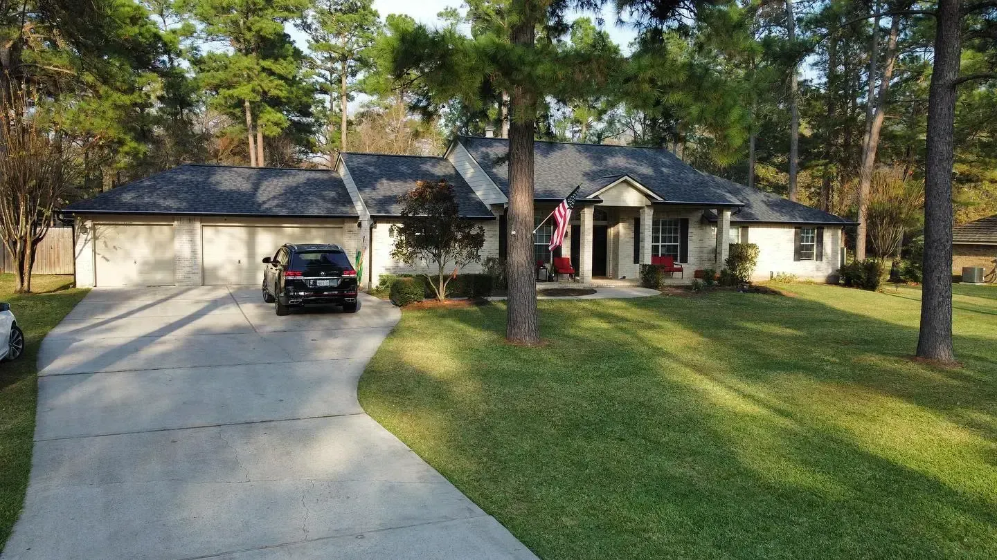 Tan house with dark roof and attached garage; car in driveway, green lawn, trees.