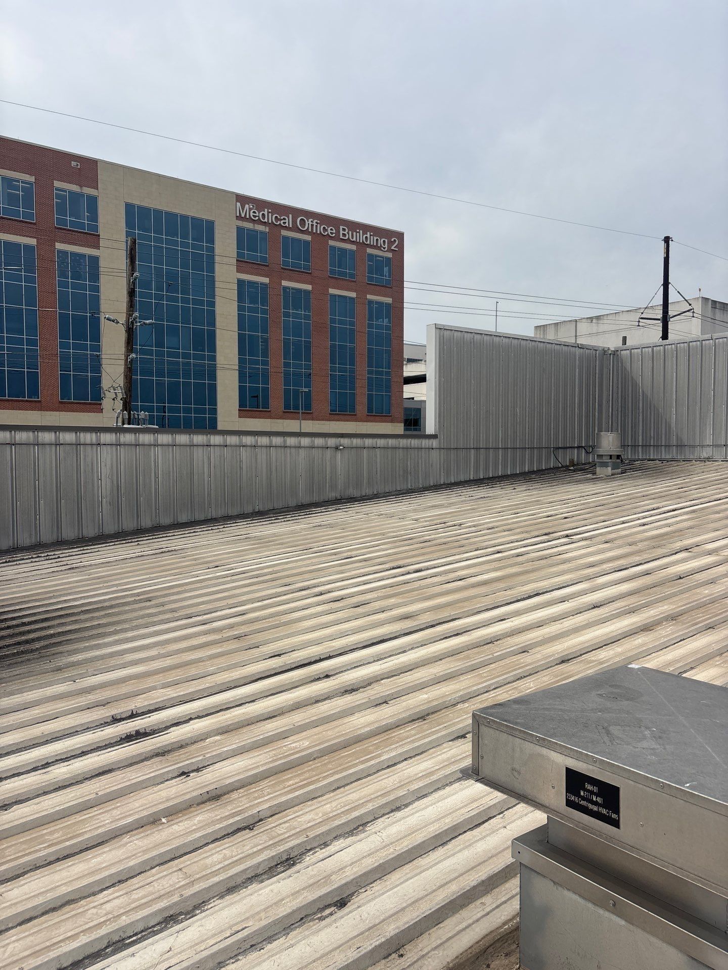 View of a corrugated metal roof with a large building featuring blue-tinted windows in the background.