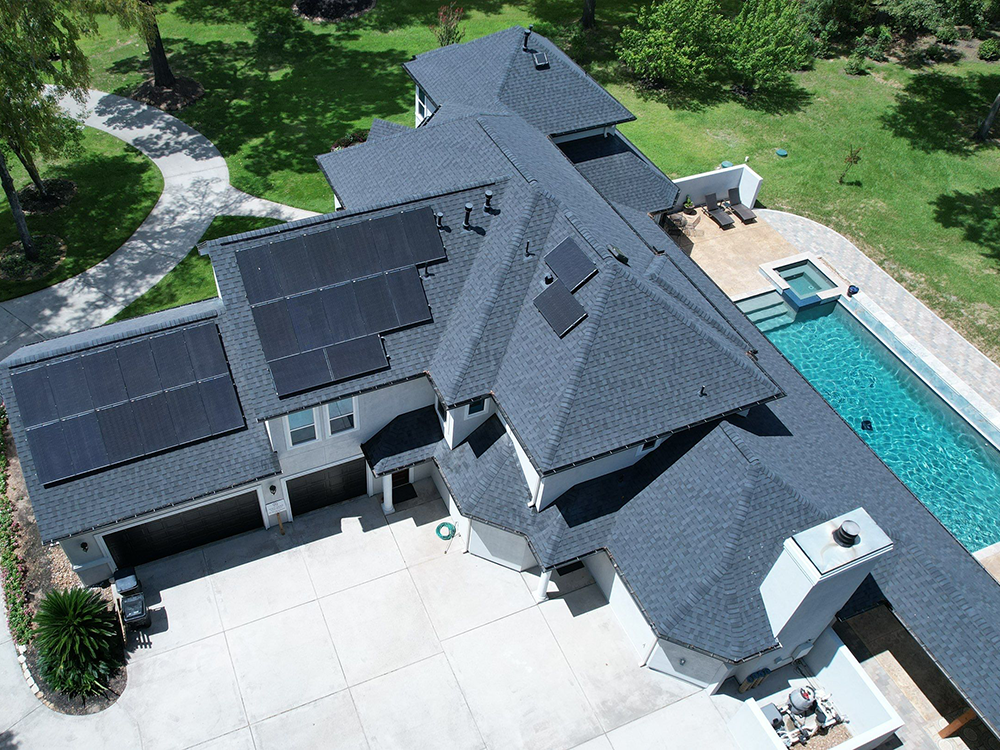 Aerial view of a large house with solar panels on the roof, a pool, and a winding walkway.