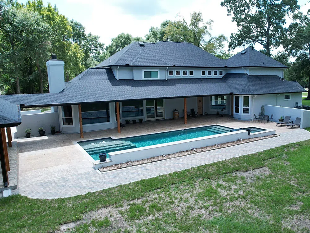 A large house with a pool in the backyard. The house is light grey with a dark grey roof.