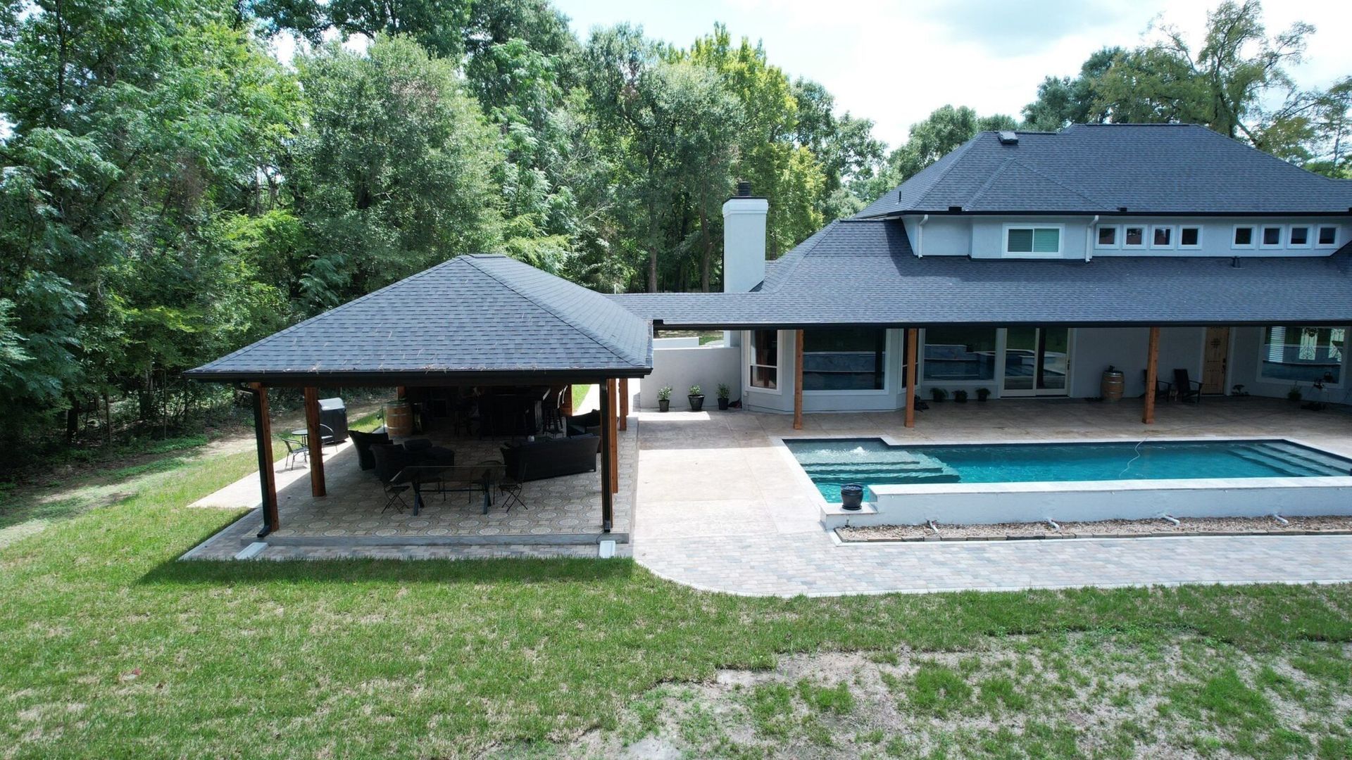 Backyard with a pool, gazebo, and modern house with a dark roof and a green lawn.