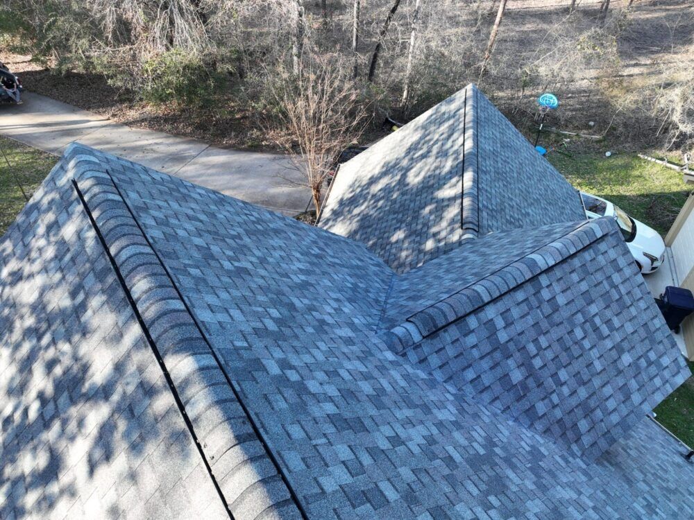 View of a gray shingle roof, surrounded by trees and a driveway.