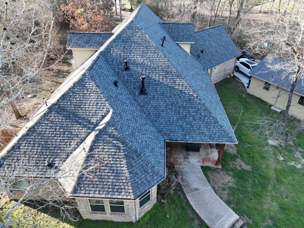 Aerial view of a blue-roofed house with a curved walkway leading to the entrance. A car is parked nearby.