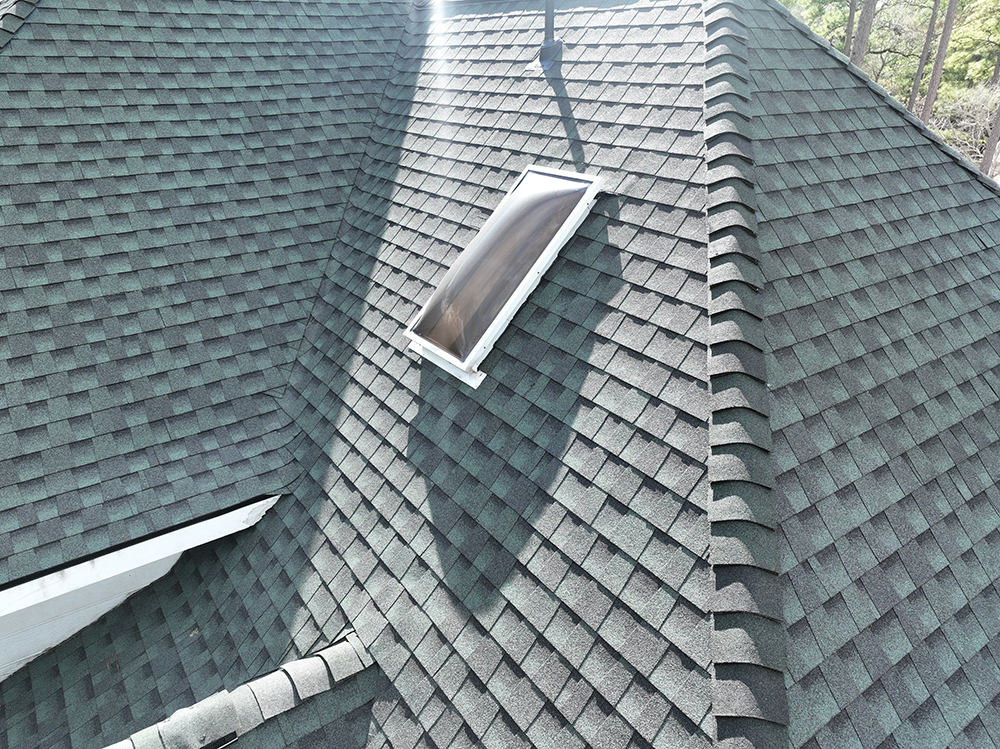 Dark gray shingle roof with a rectangular skylight and chimney.