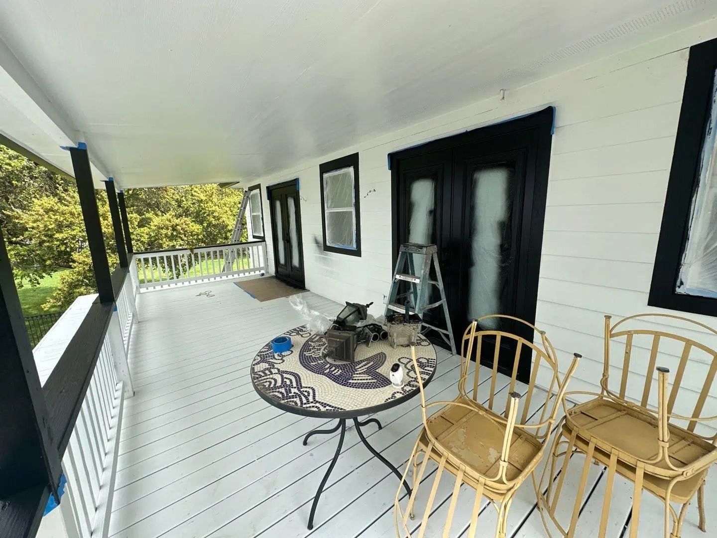 Covered porch with white ceiling and floor, black trim. Two yellow chairs sit by a round table.
