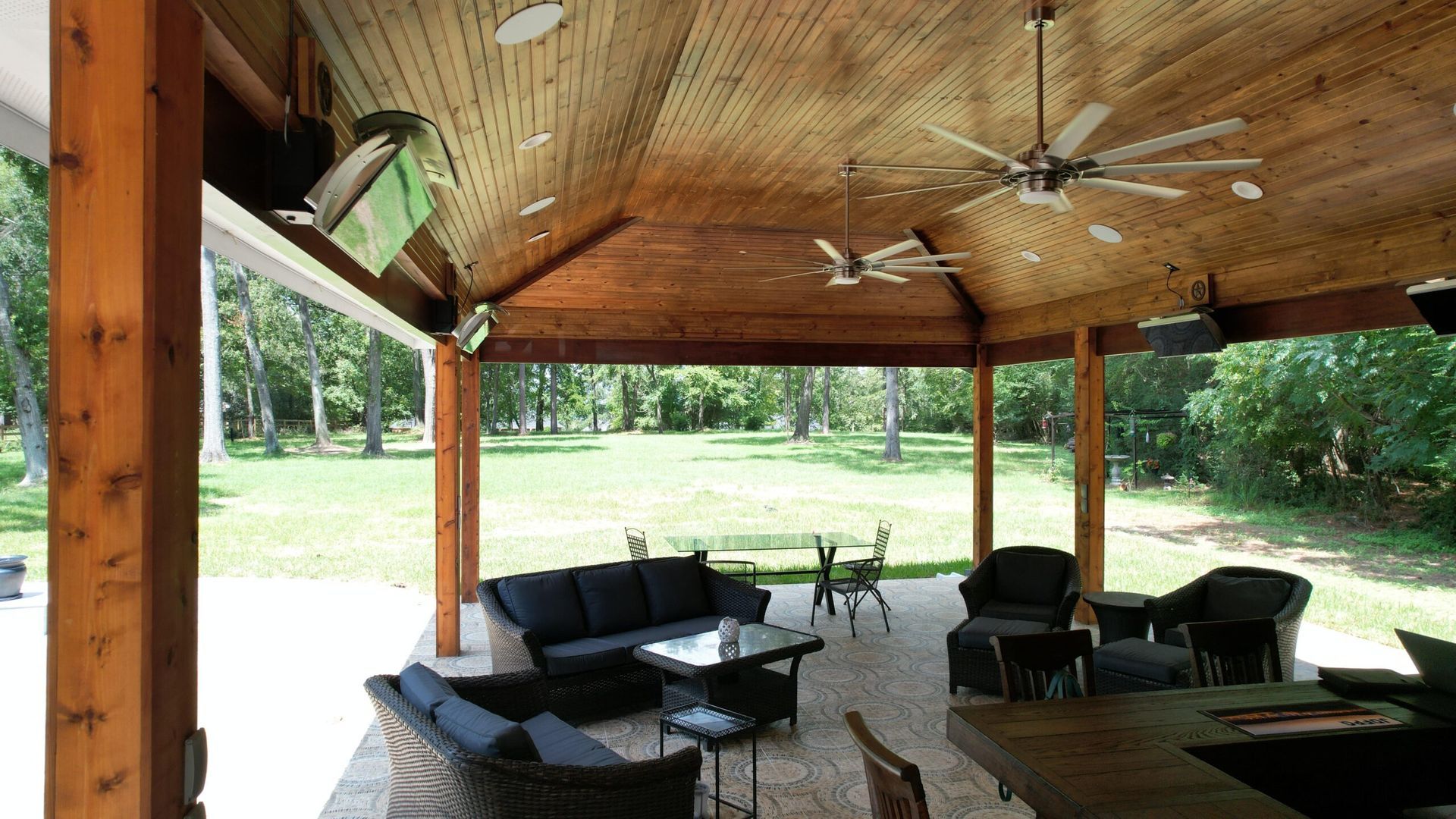 Outdoor patio with wood ceiling, seating areas, and a view of a grassy yard.