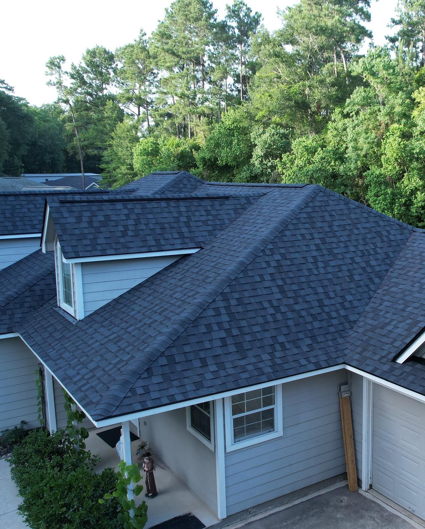 Dark blue shingled roofs of a multi-unit house, light blue siding, trees in the background.