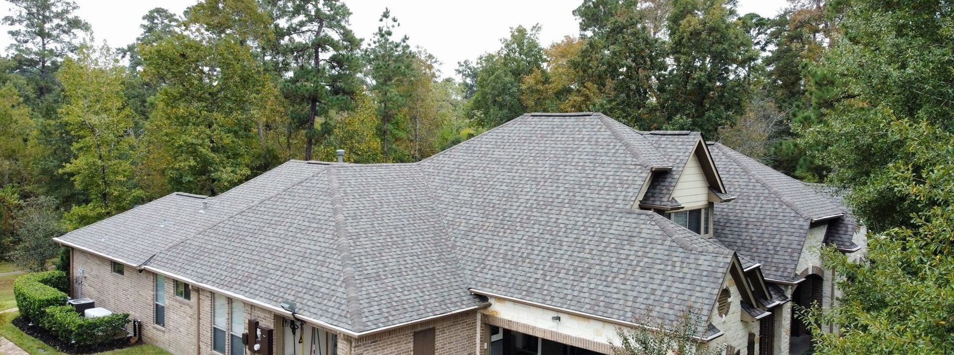 Large house with weathered gray roof surrounded by trees.