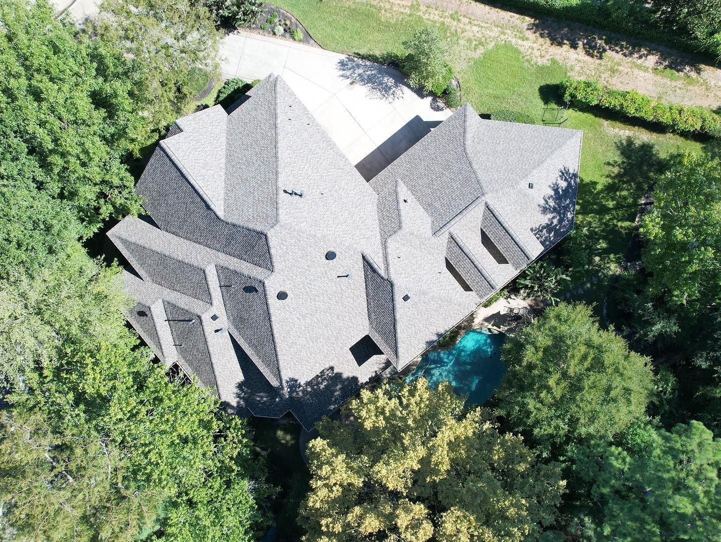 Aerial view of a gray-roofed house surrounded by trees, with a small blue pool visible.