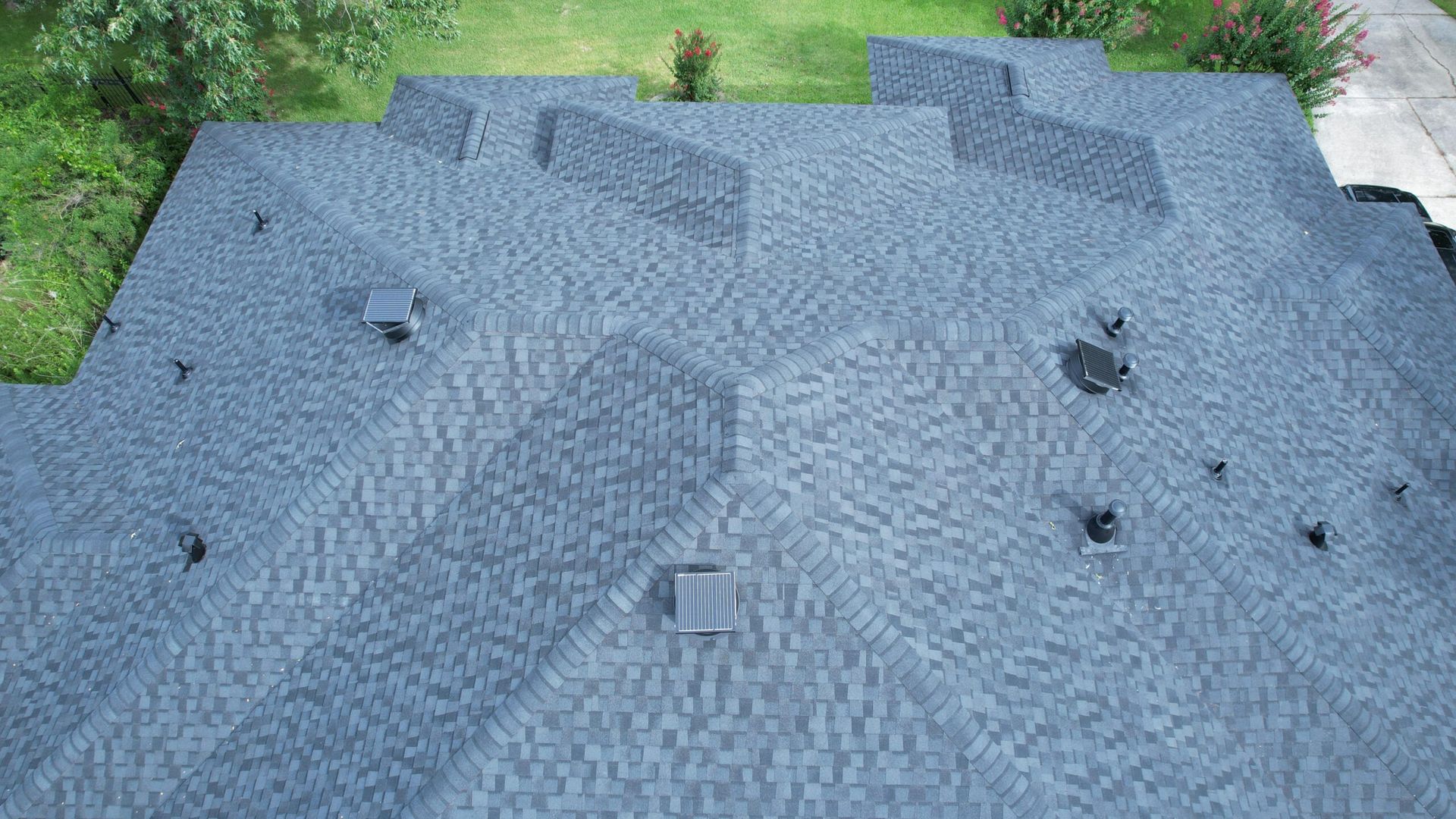 Overhead view of a dark gray shingled roof with multiple vents and geometric dormers.