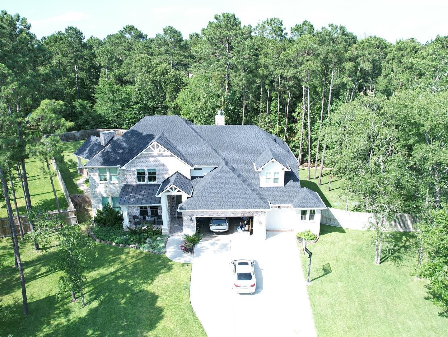 Large, white house with dark roof and attached garage; long driveway leads to the street; trees in background.