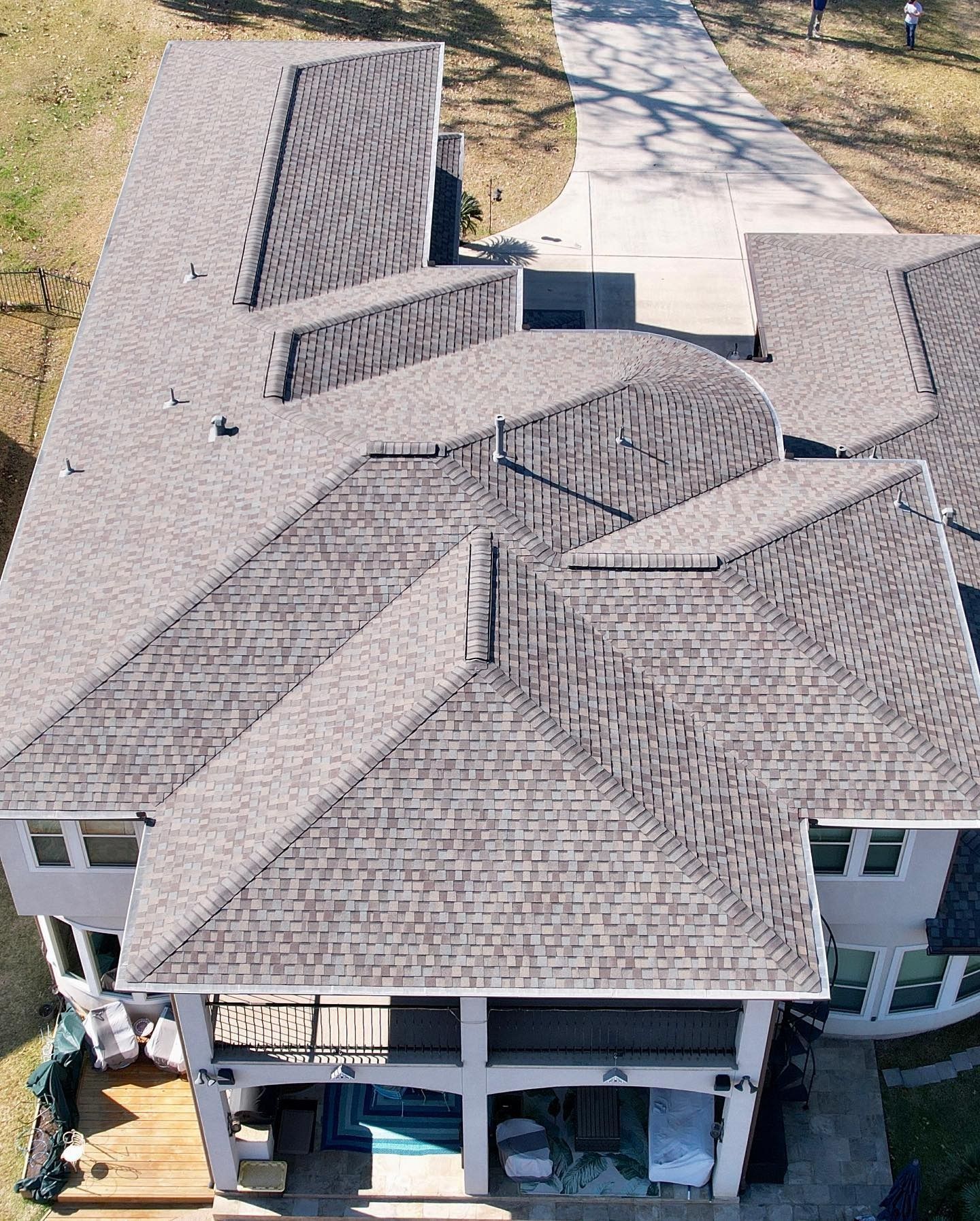 Gray shingled roof of a large house with multiple sections and a concrete driveway.